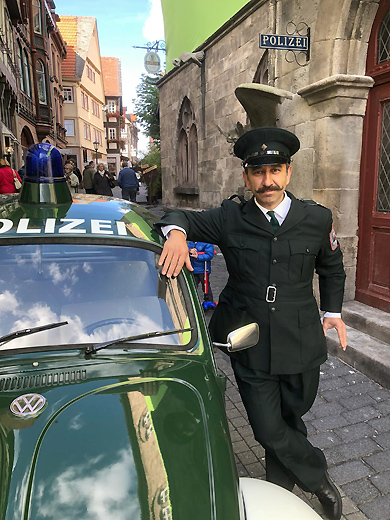 Beim Dreh zu "Die Wolf-Gäng" in der historischen Altstadt von Alsfeld steht Schauspieler Hilmi Sözer vor der dortigen Polizeiwache neben seinem Polizei-Einsatzfahrzeug, dem VW Käfer aus dem Polizeioldtimer Museum in Marburg.